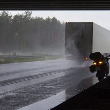 Stovintis motociklas lenkiamas sunkvežinio lyjant stipriam lietui
