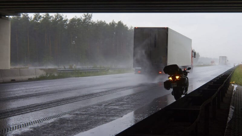 Stovintis motociklas lenkiamas sunkvežinio lyjant stipriam lietui