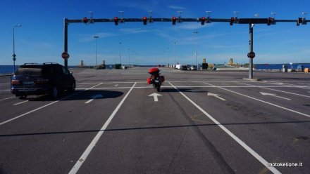 Raudonas motociklas stovi beveik tuščiame kelyje prie raudono šviesoforo
