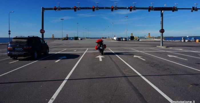 Raudonas motociklas stovi beveik tuščiame kelyje prie raudono šviesoforo